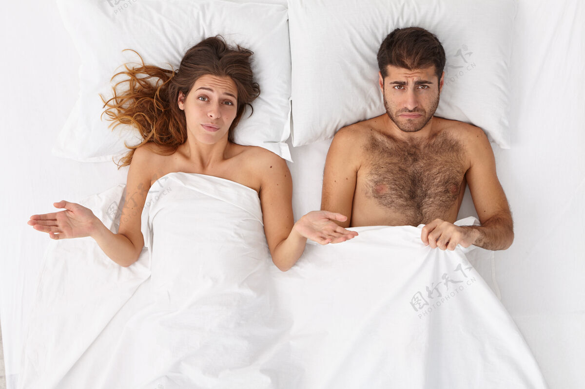 性头顶镜头中困惑的女人和她的丈夫在床上有性问题 不高兴的表情 躺在白毯子下男人有阳痿 勃起失败日常生活家庭问题观念顶消极离婚