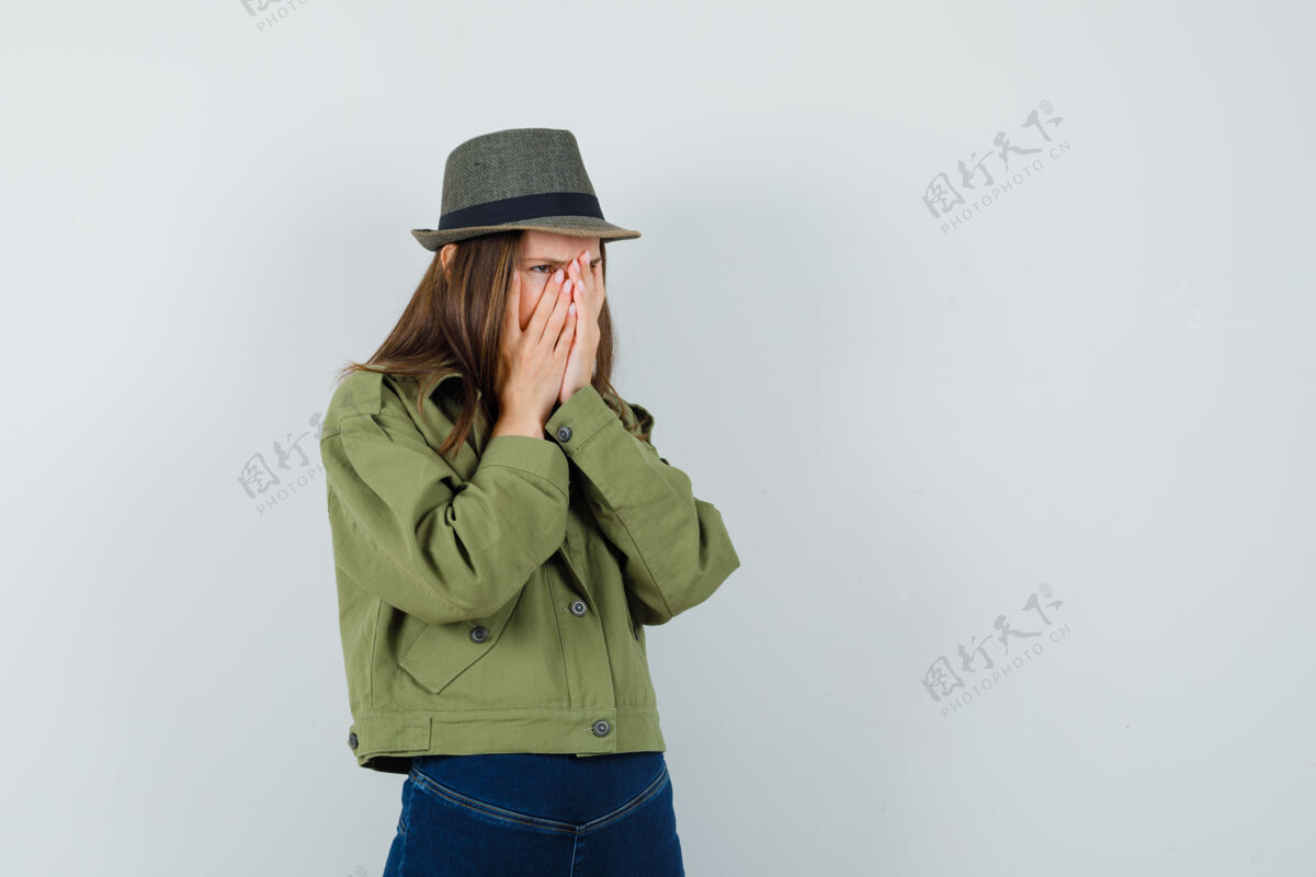 夹克年轻的女士手放在脸上穿着夹克裤子帽子 看起来很苦恼手连衣裙帽子