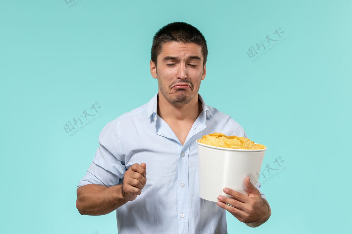 男人正面图：年轻人拿着篮子 手里拿着土豆 在淡蓝色的墙上看电影外套土豆观看