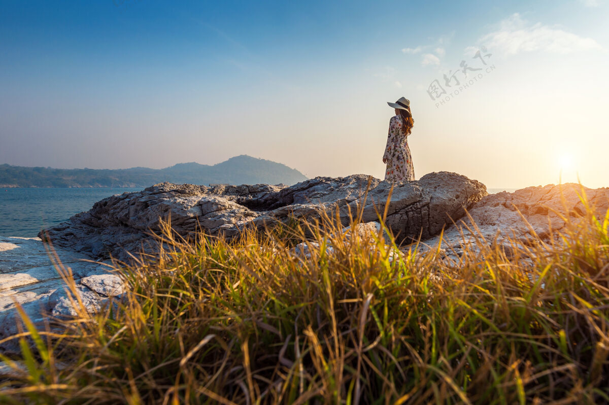 亚洲夕阳下站在四长岛岩石顶上的年轻女子背包岛屿冒险