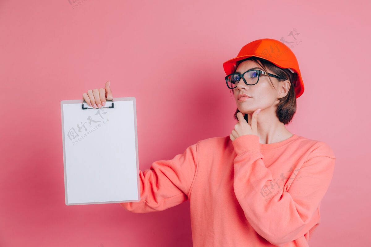 成人漂亮体贴的女建筑工人拿着白色的空白标牌 背景是粉色的戴着建筑头盔女性工人模型