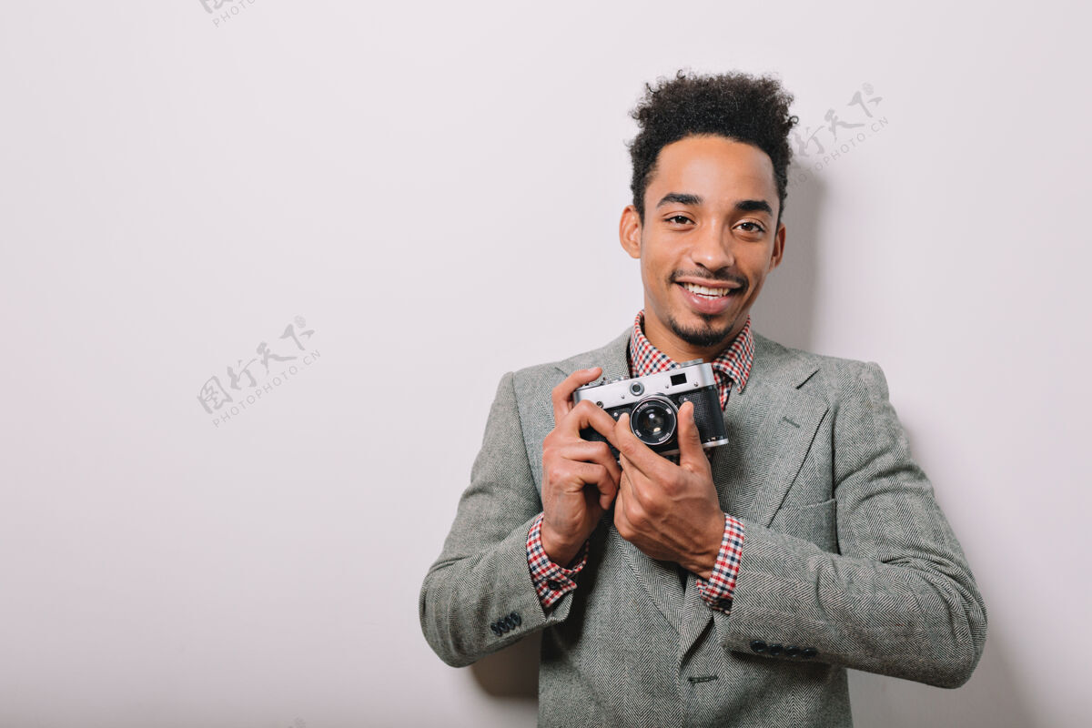 男人室内写真的快乐的非裔美国男性穿着灰色夹克手持相机在灰色的手上时尚表情欢呼