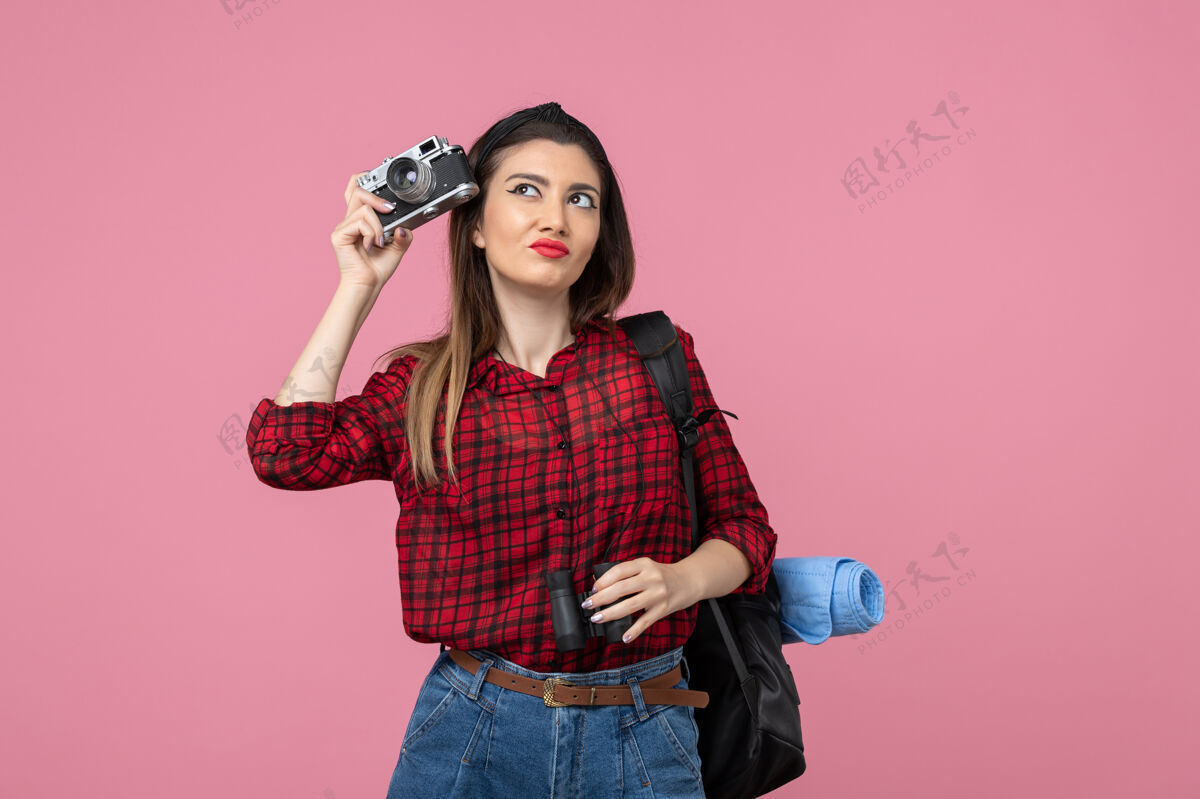 肖像前视图年轻女性用双筒望远镜和相机对一个粉红色背景色的女人人类相机微笑漂亮