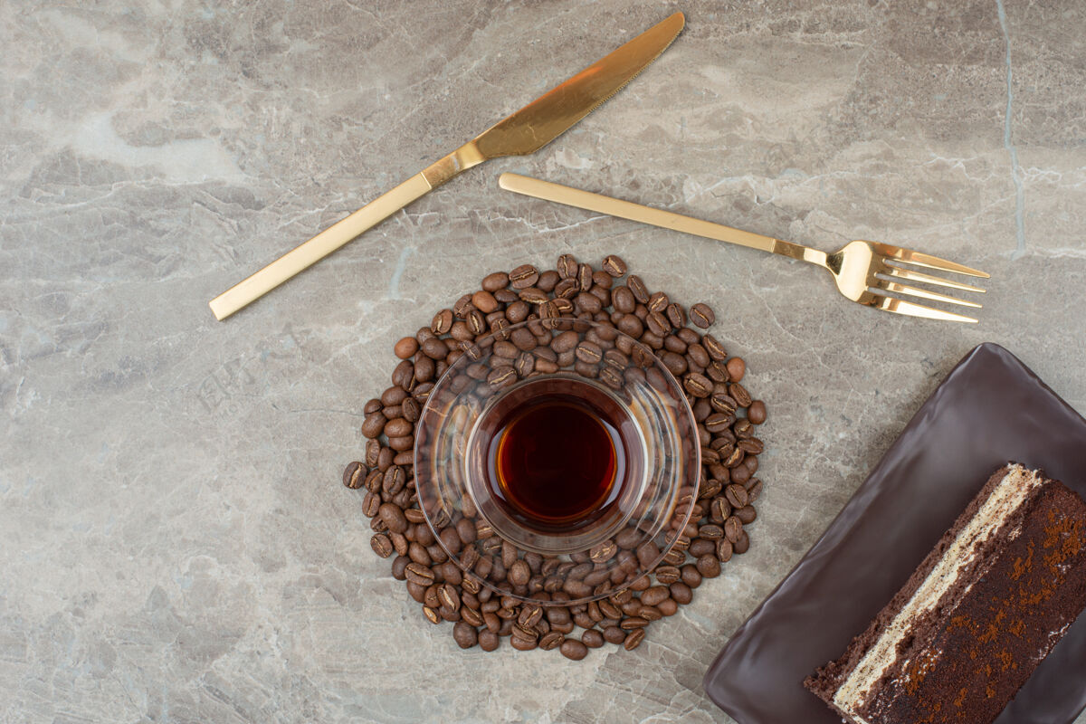蛋糕在大理石桌上放一片巧克力蛋糕 咖啡豆和一杯茶餐具巧克力咖啡豆
