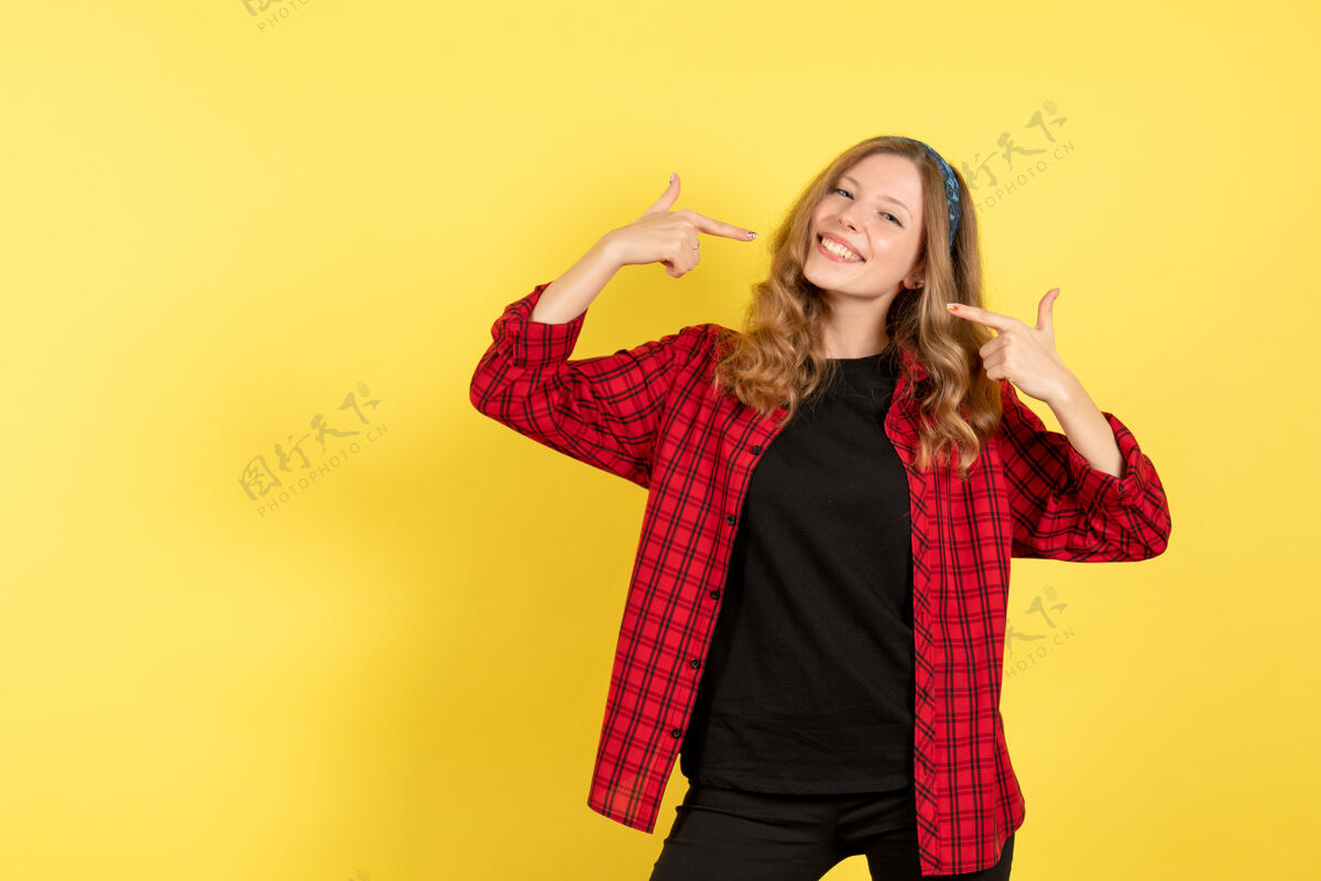 肖像正面图穿着红色格子衬衫的年轻女性在黄色背景上微笑着摆姿势人类女孩情感色彩模特女人人类衬衫微笑