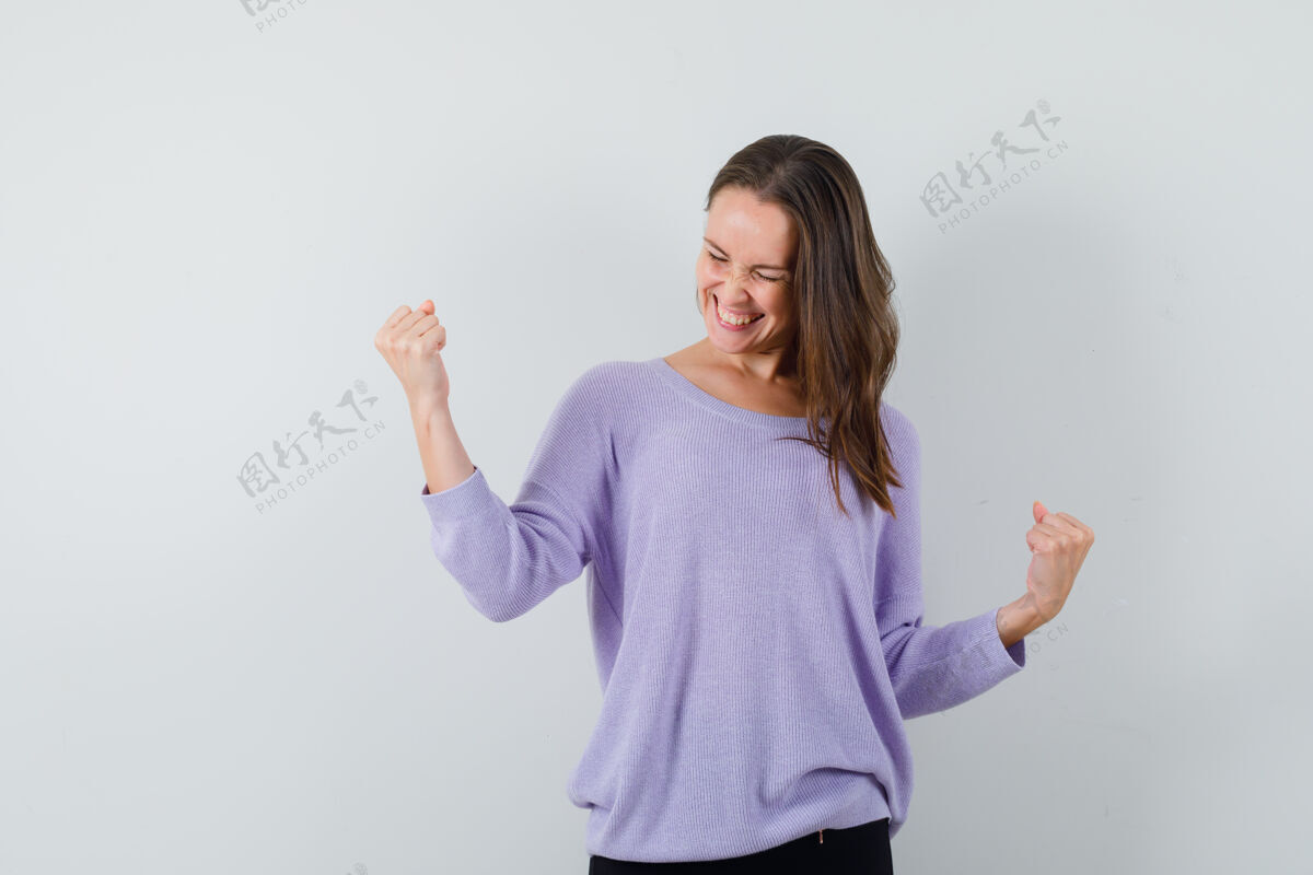 展示身着淡紫色上衣的年轻女性 展现出赢家的姿态 看起来很开心头发卷发女士