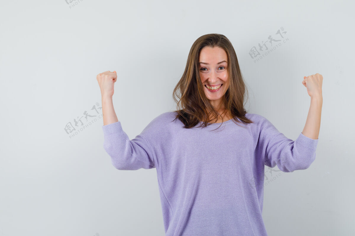 自信年轻的女性举起双臂 身着淡紫色上衣展示获奖者的姿态 看上去很开心正面图举起手势化妆