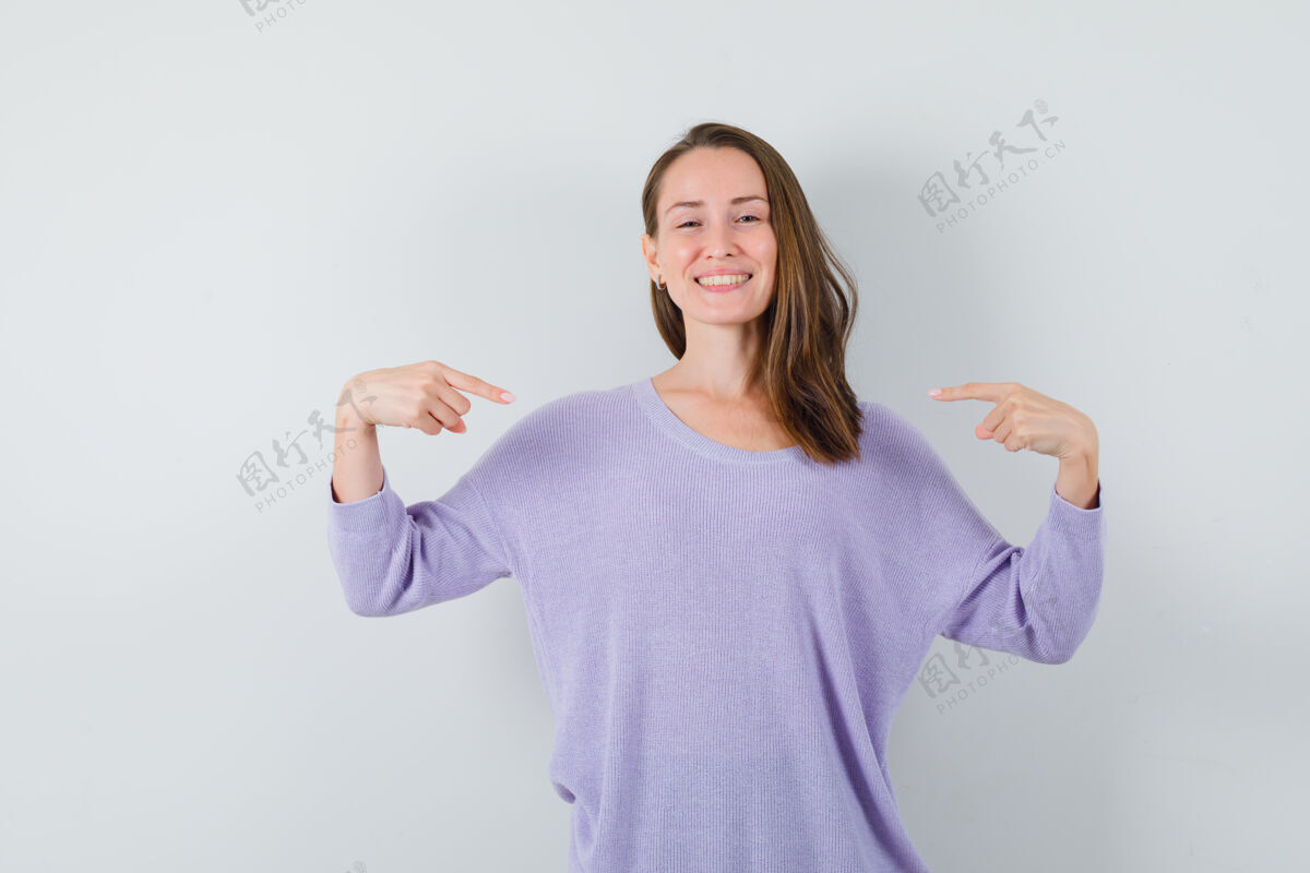 头发年轻女子指着自己在淡紫色衬衫 看起来乐观前视图她自己女士女性