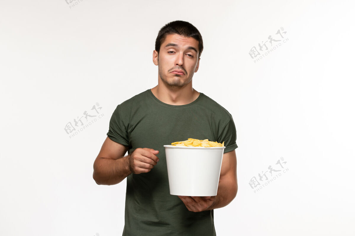 电影正面图身穿绿色t恤的年轻男性 带着土豆cips 在白墙上看电影 男人孤独的电影院观看咖啡杯子