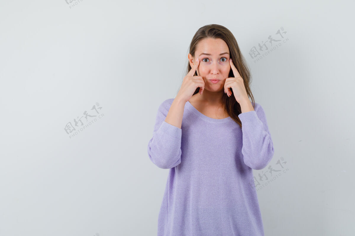 女性年轻的女性指着她的眼睛在淡紫色衬衫 并期待着集中前视图文本空间手衬衫卷发