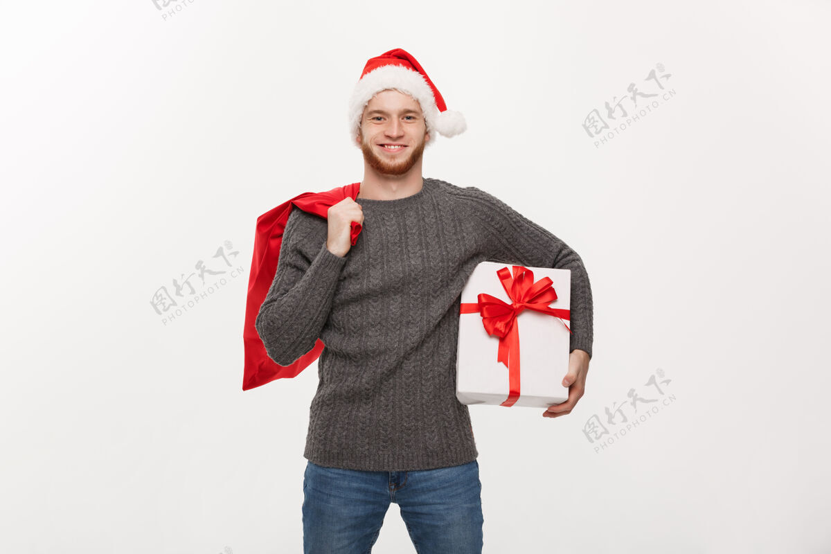 节日年轻的快乐胡子男人拿着圣诞老人包和白色礼物大诺埃尔胡须