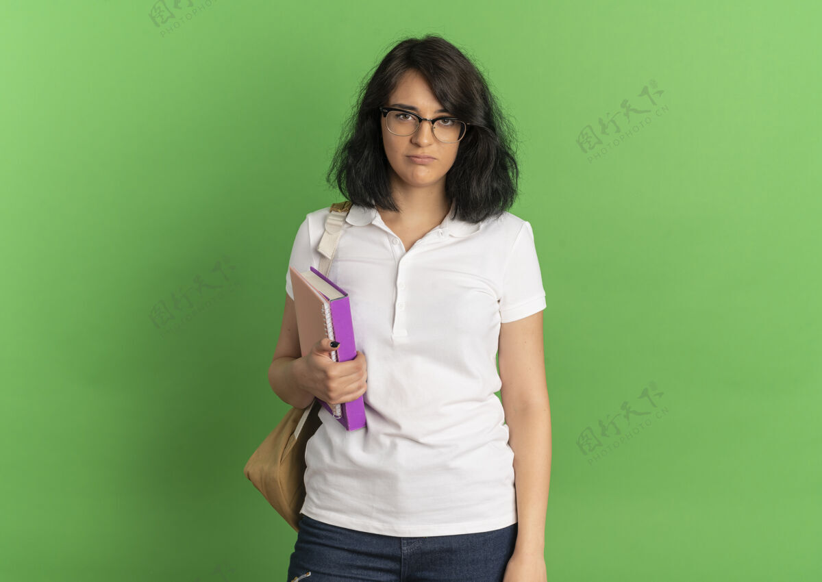 绿色年轻漂亮的白人女生戴着眼镜 背着书包站在绿色的书架上拿着书 还有复印空间穿包眼镜
