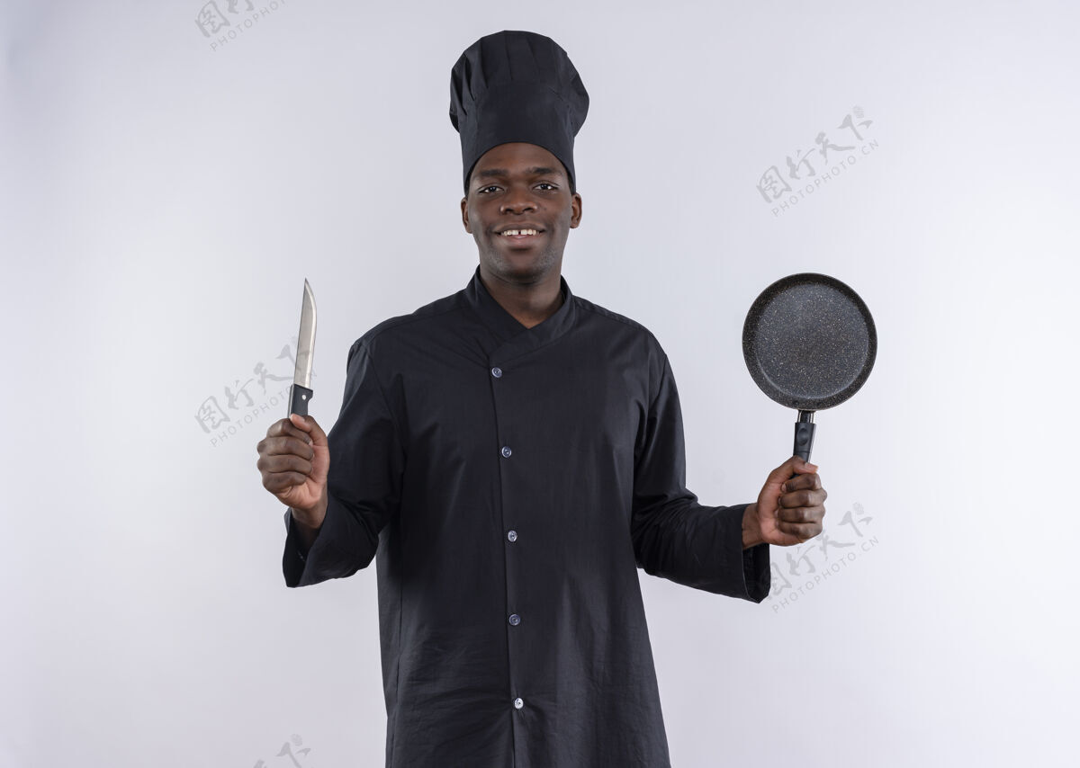 年轻身着厨师制服的年轻美籍黑人厨师手持小刀和煎锅 放在白色地板上 留有复印空间非裔美国人刀平底锅