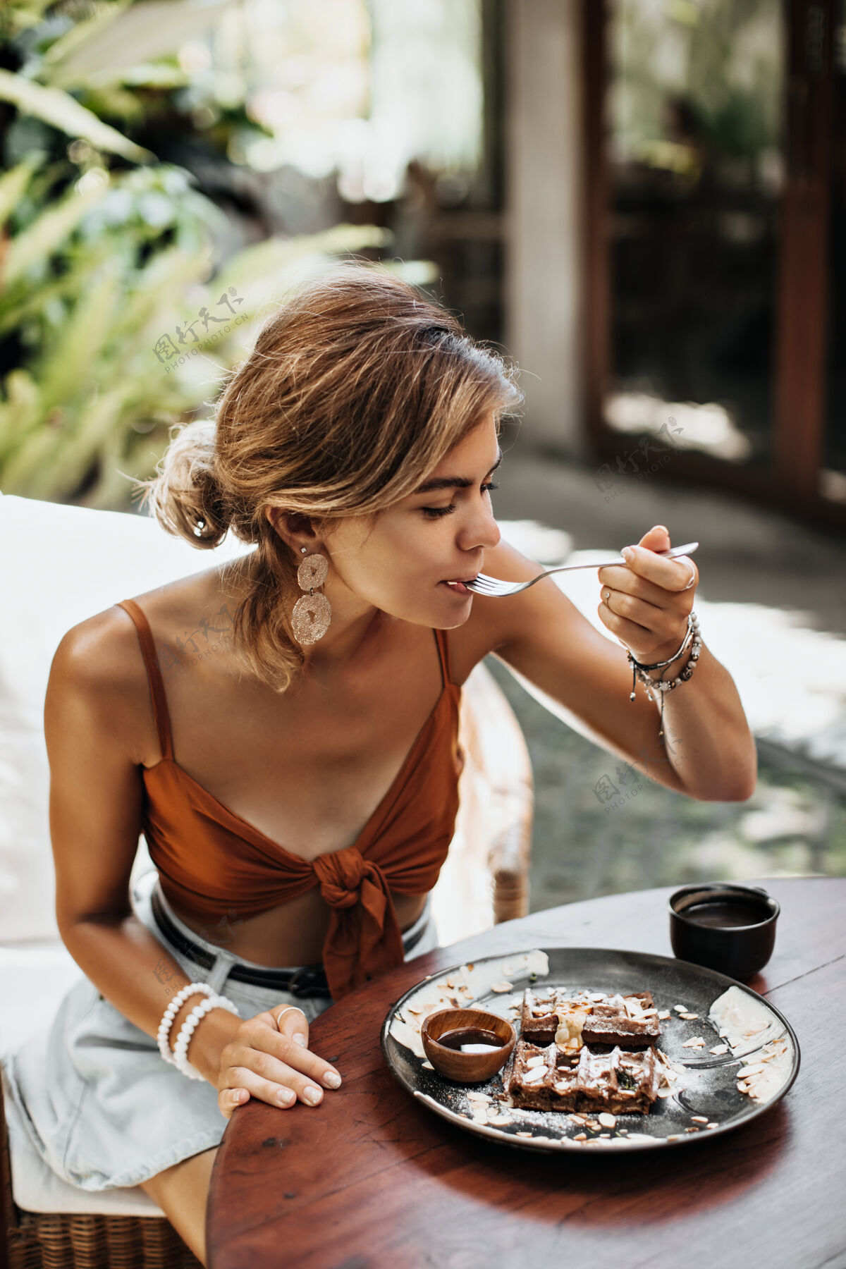 黑发穿着棕色胸罩和牛仔短裤的金发迷人女人吃着奶油和巧克力酱的华夫饼 享受着它的味道夏天热带女性