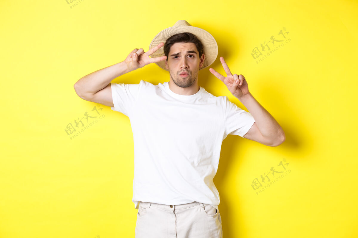 成人旅游度假的概念酷酷的家伙在度假时拍照 摆出和平的姿势 戴着草帽 站在黄色的背景下工作室黄色男人