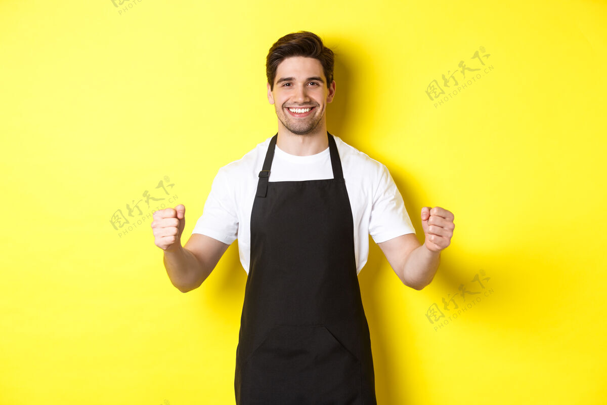 自信友好的咖啡店服务员举手站立 放置您的标志或徽标 站在黄色背景上黄色厨师时尚