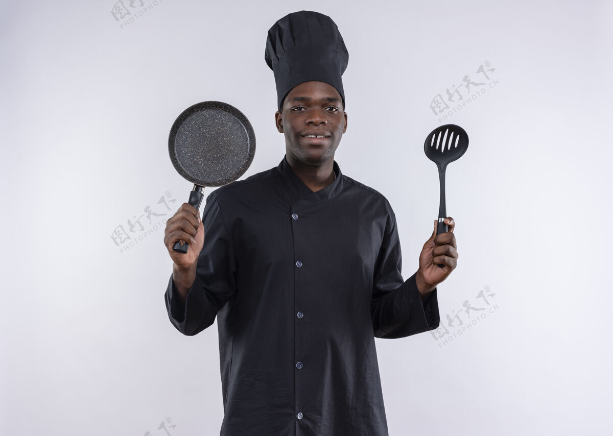 烹饪年轻的美籍黑人厨师身着厨师制服 手拿煎锅和锅铲 放在白色的地板上 留有复印空间厨师年轻副本