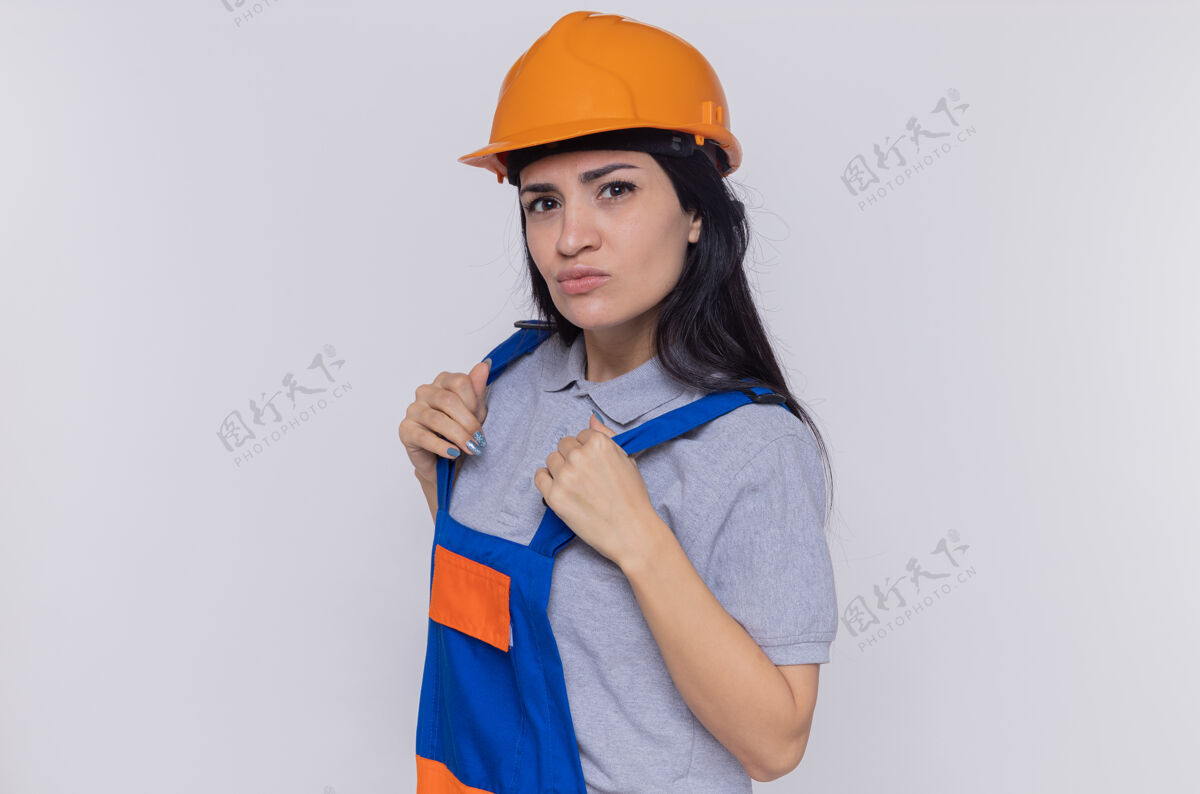 建设者身穿施工制服 头戴安全帽的年轻建筑妇女站在白色的墙上 神情严肃自信地看着前方自信站立表情