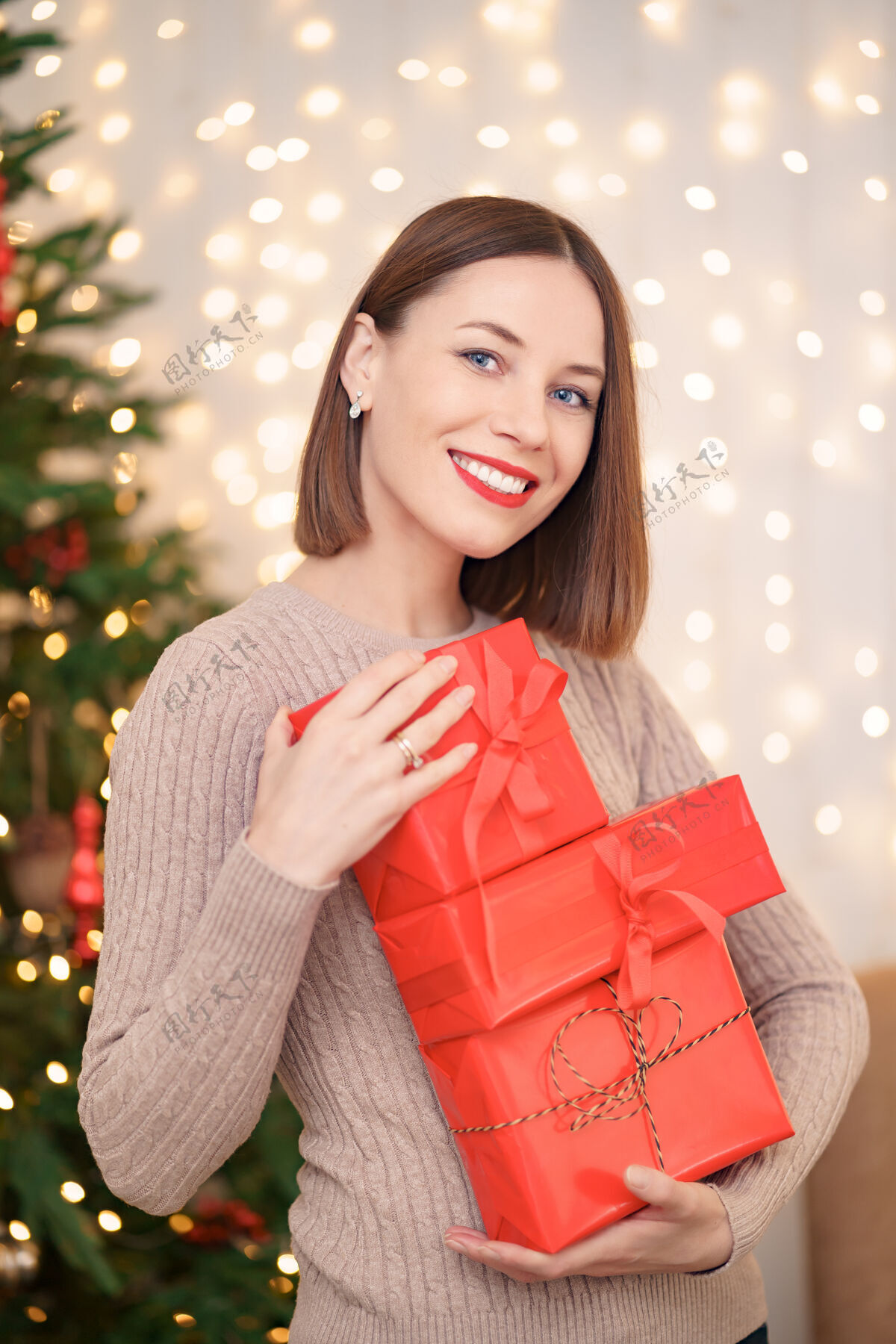 光泽快乐的年轻女子拿着许多圣诞树和圣诞灯的礼物盒红唇女性盒子