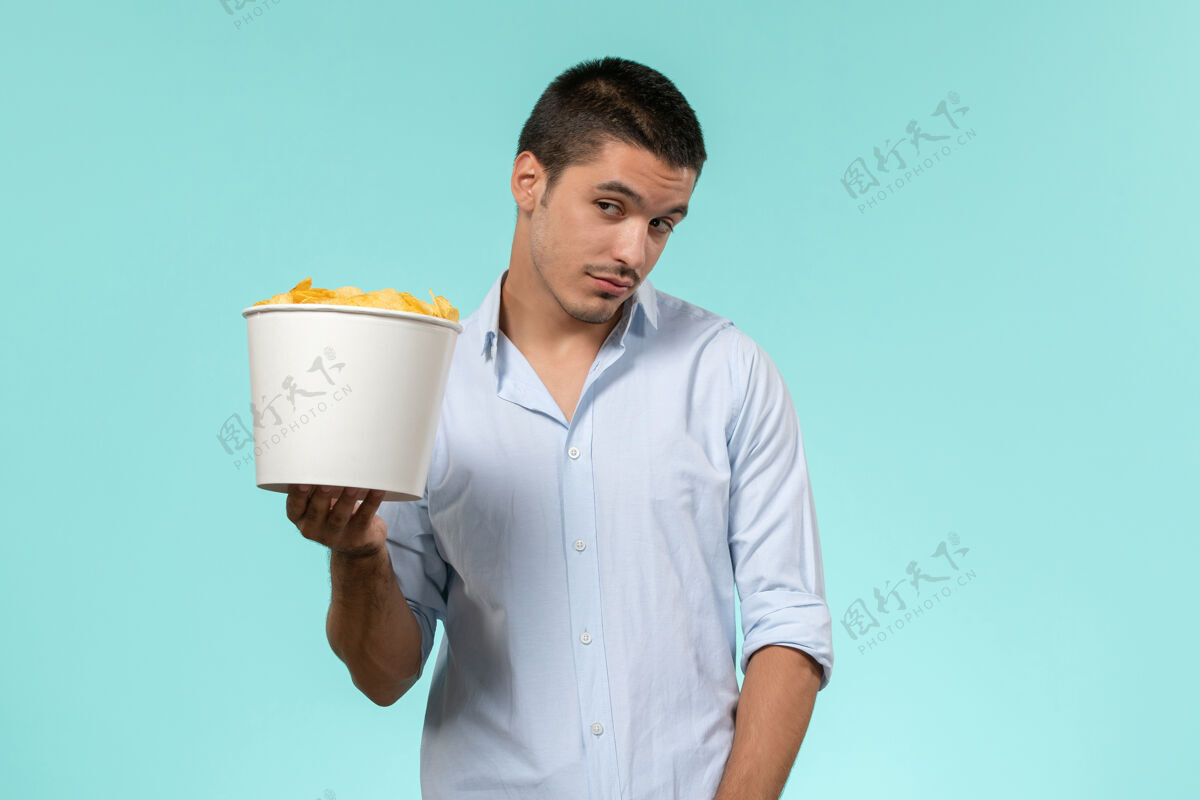 喝正面图：年轻的男性拿着蓝面薯片的篮子拿篮子容器