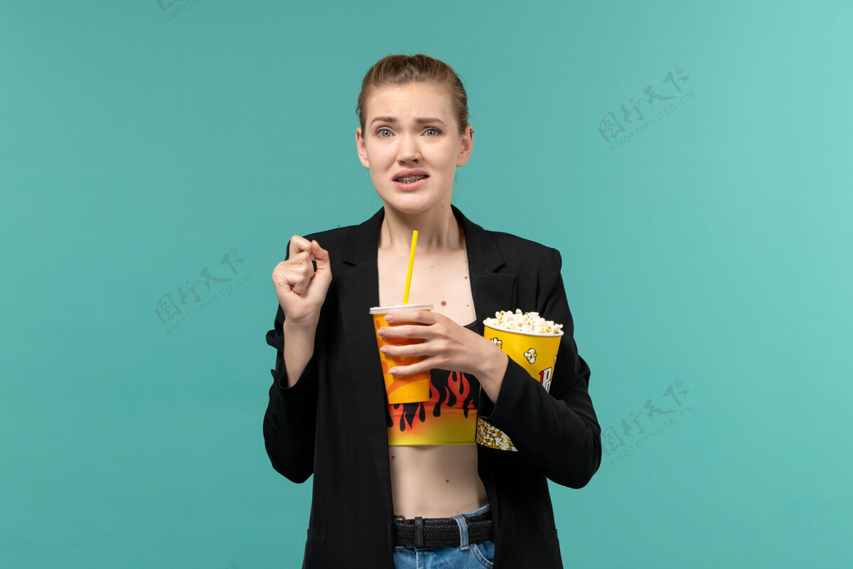 剧院正面图：年轻女性拿着爆米花喝酒 在浅蓝色的表面上看电影男电影院西装