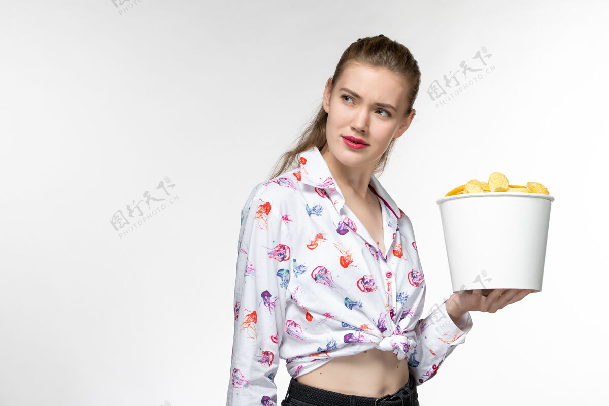 抱正面图：白色表面上拿着薯片的年轻女性篮子篮子年轻女性衣服