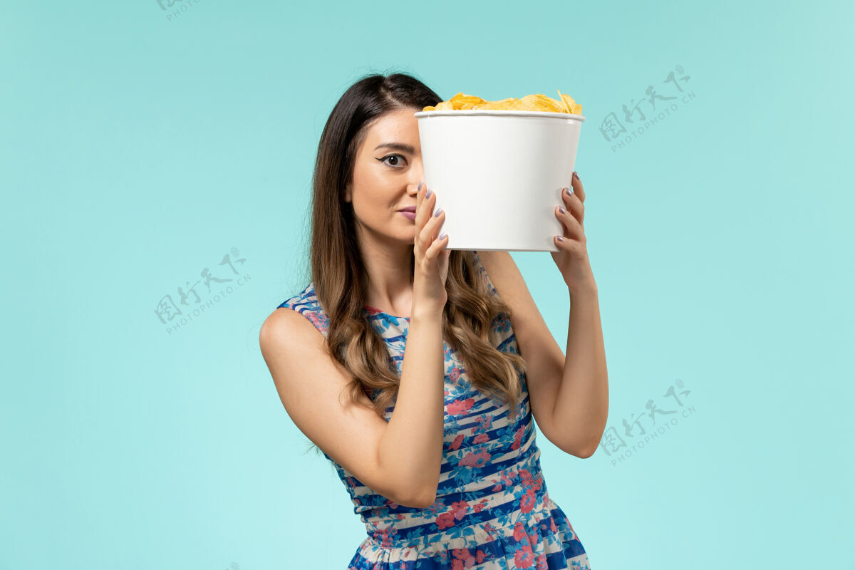 女性正面图：蓝色桌子上拿着薯片的年轻女性篮子电影篮子电影