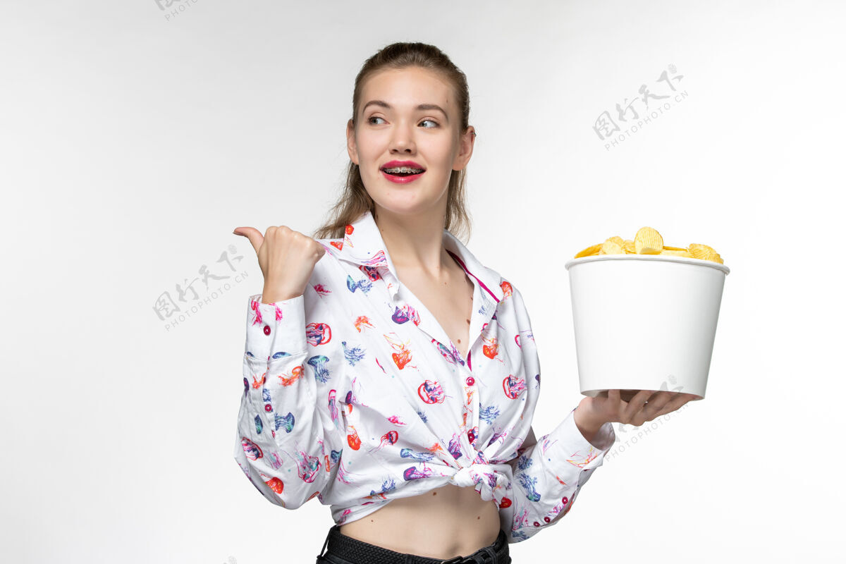 享受正面图：年轻的女性拿着篮子和薯片 在白色的表面上微笑抱孤独家庭主妇