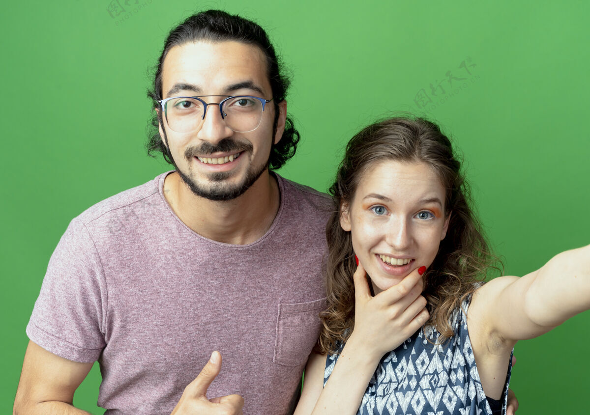 夫妇一对年轻的男女 站在绿色的墙上 面带幸福的笑容看男人微笑