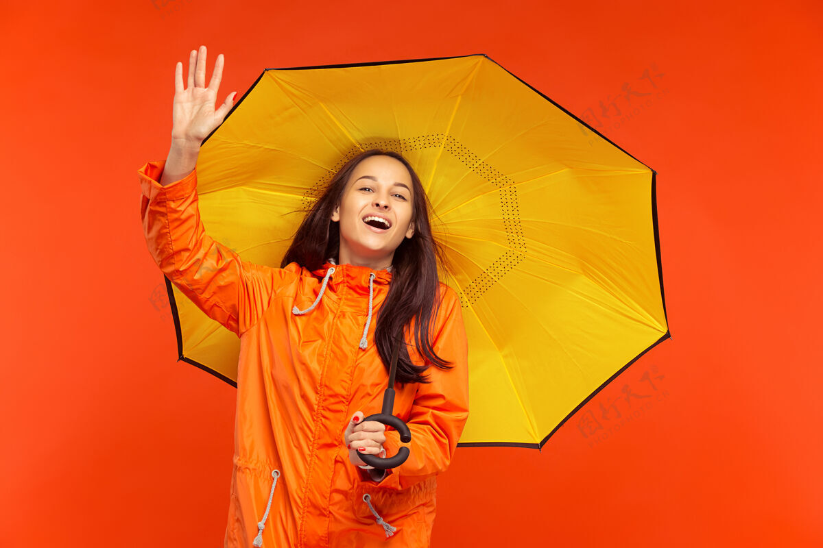 安全那个快乐微笑的小女孩穿着秋天的橘色夹克在摄影棚摆姿势 孤立在橘色的墙上肖像冻结秋天