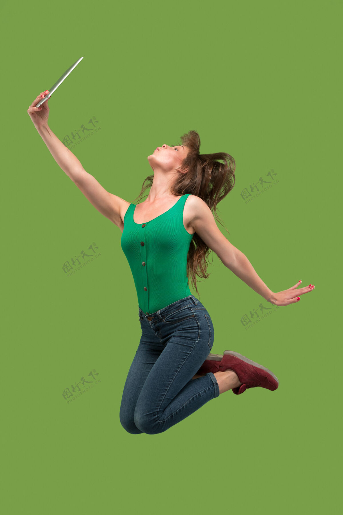 休闲年轻女子跳伞时使用笔记本电脑或平板电脑小玩意跳过绿色工作室背景运动持有携带