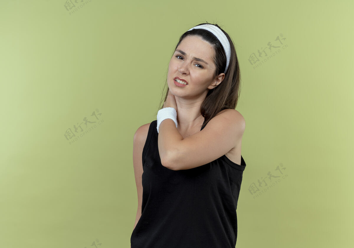 健身戴着头巾的年轻健身女士站在轻质墙上摸着脖子感到不舒服不适年轻轻