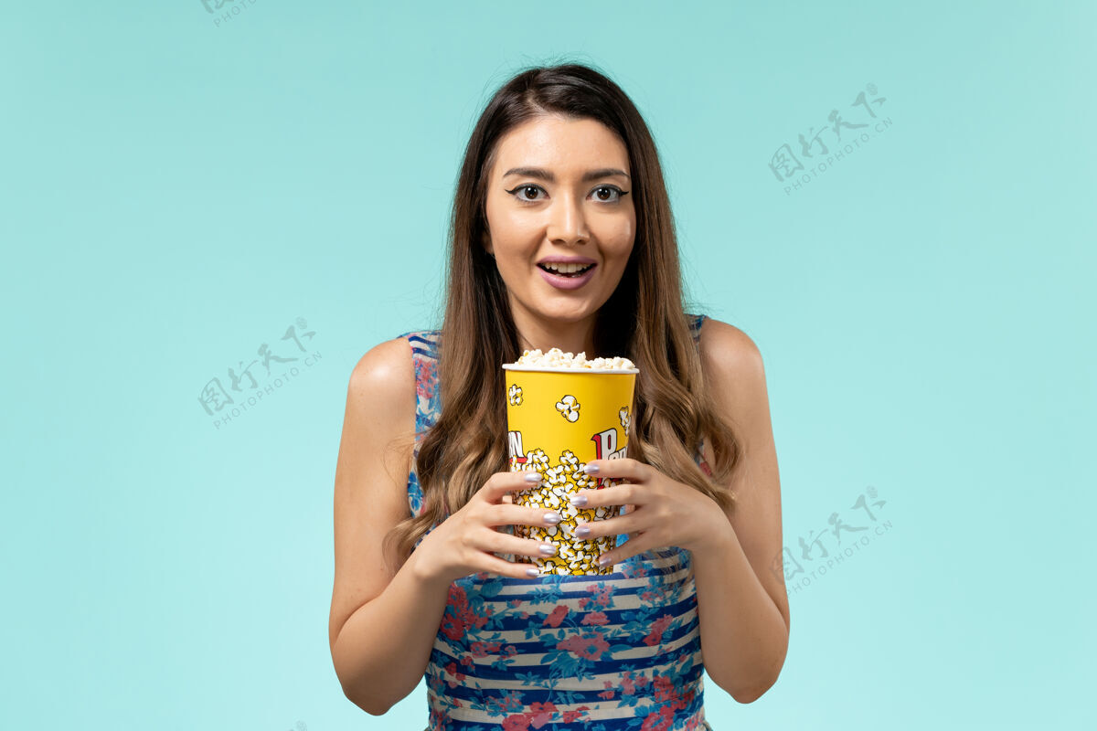 电影正面图年轻的女性拿着爆米花包在蓝色的表面上女士举行电影院