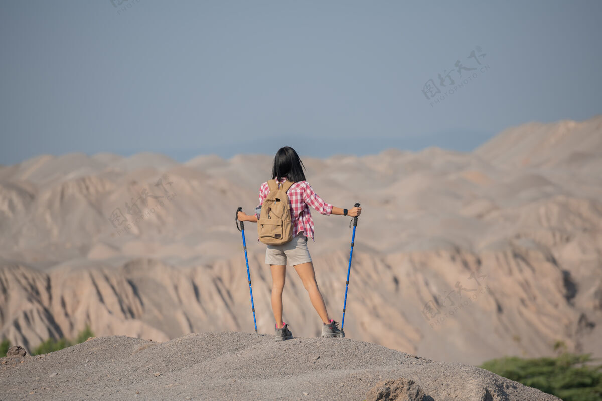 极点适合年轻女子徒步在山上站在岩石山顶山脊与背包和杆眺望风景太阳悬崖极限