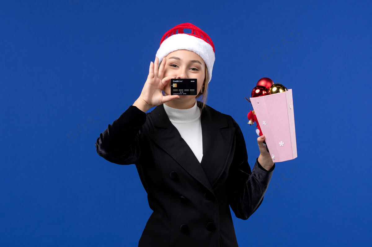 西装前视图：带着圣诞树玩具和银行卡的年轻女士在蓝色墙壁上过年前面小姐女人