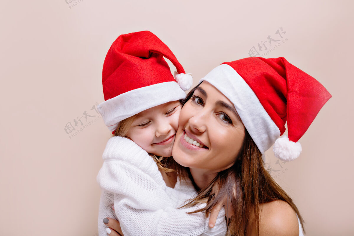人快乐 微笑 有趣的母女俩戴着圣诞老人帽摆姿势 抱着脸圣诞老人妈妈人