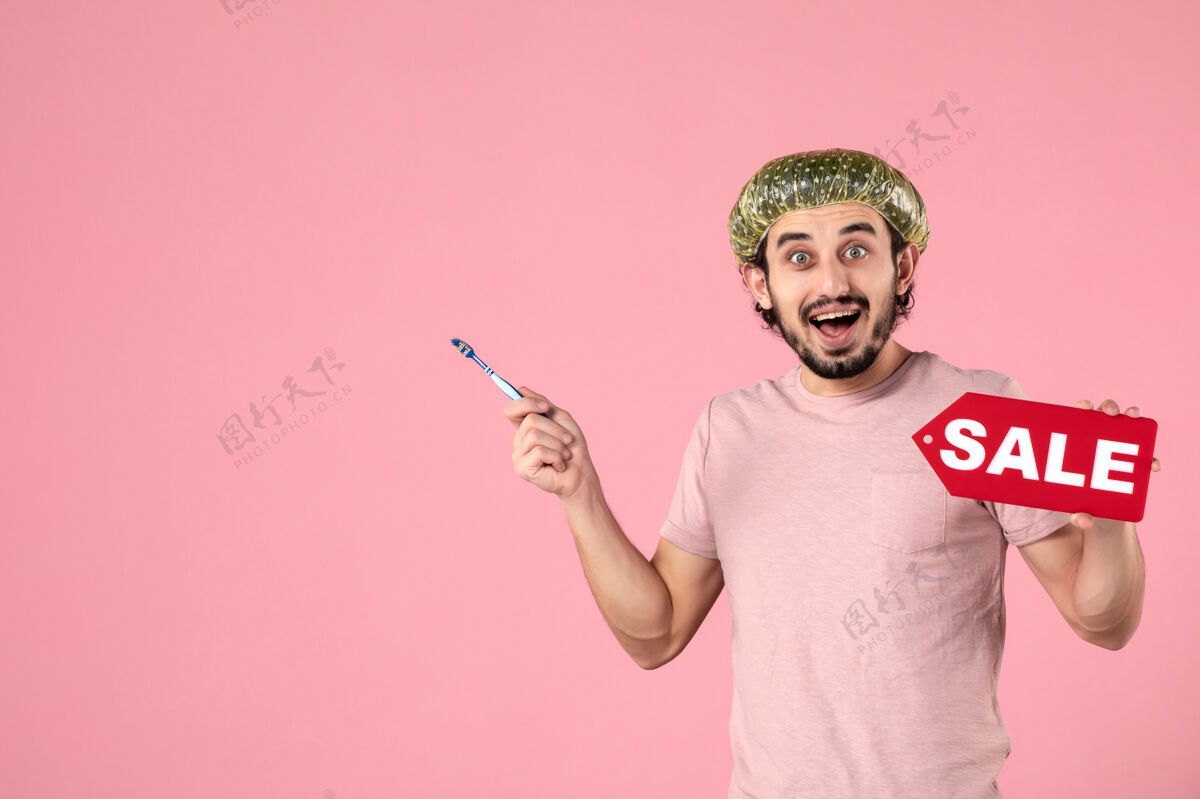 牙刷正面图年轻的男性正在清洁他的牙齿 拿着粉红色背景上的销售铭牌正面销售清洁
