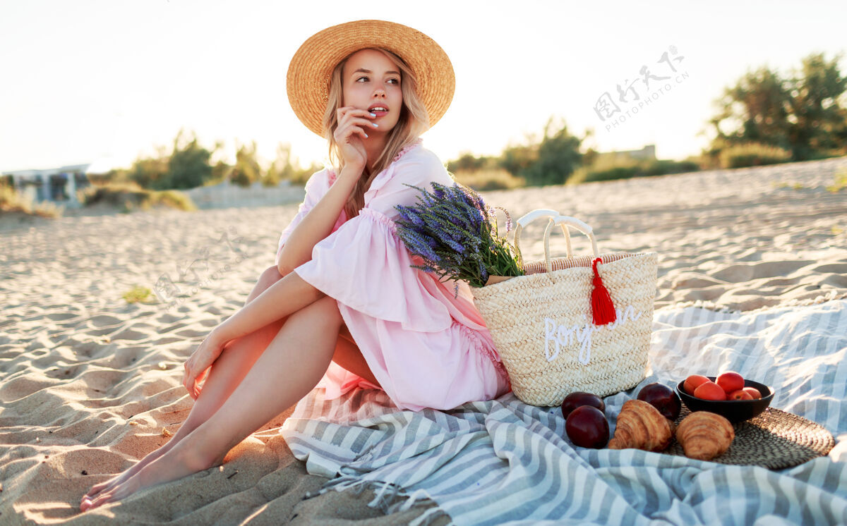 户外在海边的乡间野餐优雅的年轻女子 金色卷发 穿着优雅的粉色连衣裙 享受假期 吃水果微笑女性休息
