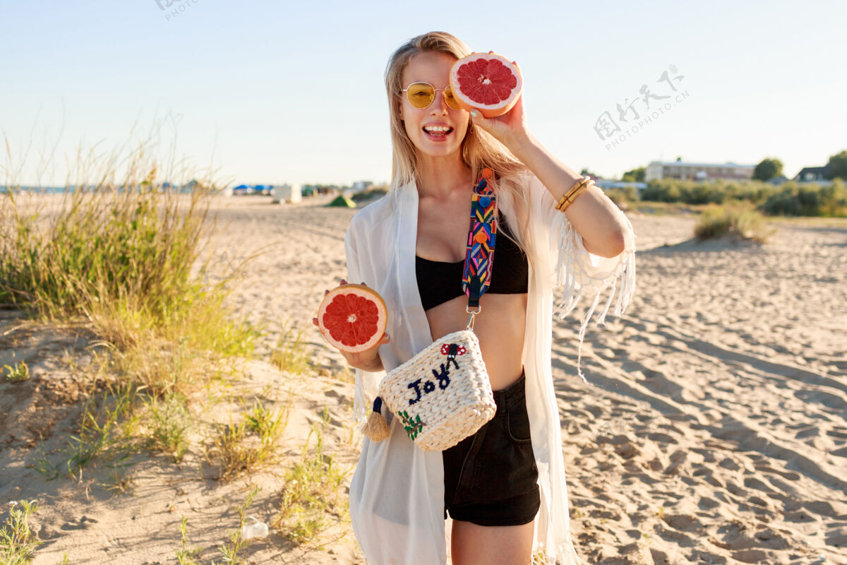 柑橘夏日写真 俏皮无忧无虑的女人手拿美味的柚子摆姿势海岸新鲜自然