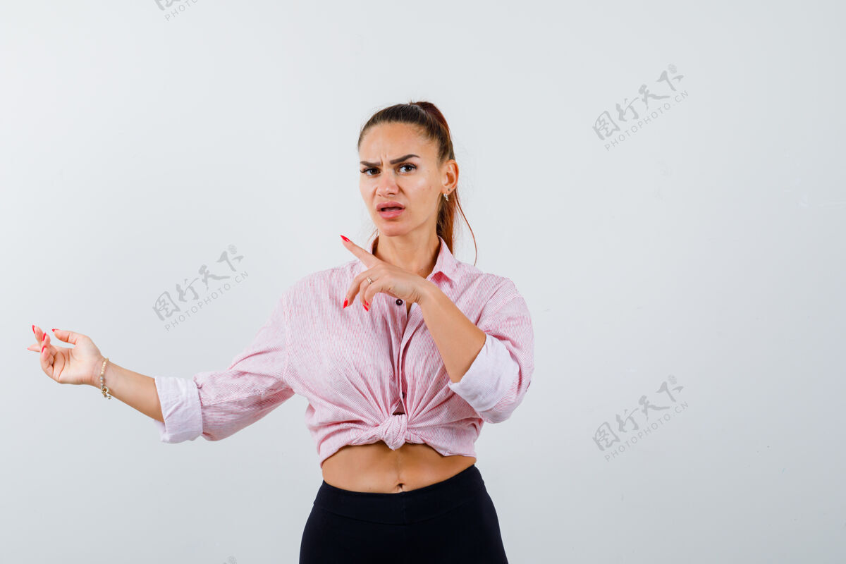 模型年轻的女士指着左边的衬衫 裤子和关注前视图指向女人户外