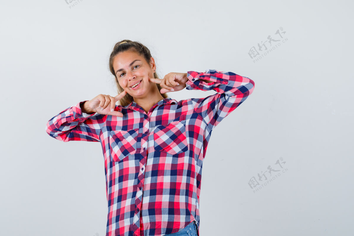 女性穿着格子衬衫的年轻女士手指放在脸颊上 看上去很愉快正面图自然成人微笑