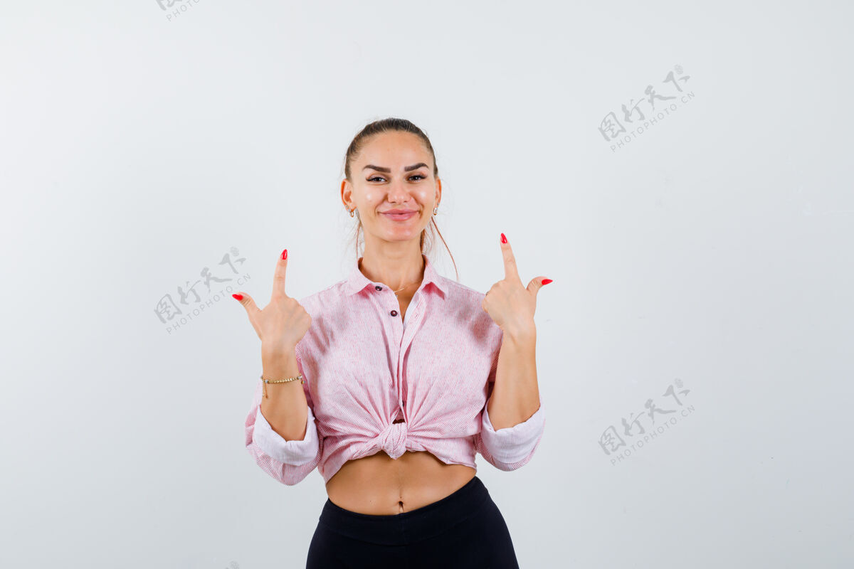 衬衫年轻的女士指着衬衫 裤子和看起来活泼前视图欢呼时尚快乐