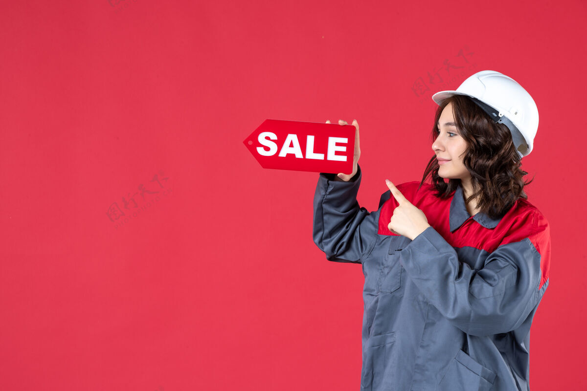 硬正面近距离观看身着制服 戴着安全帽 指着隔离红墙上的销售图标的快乐女工成人业务指向