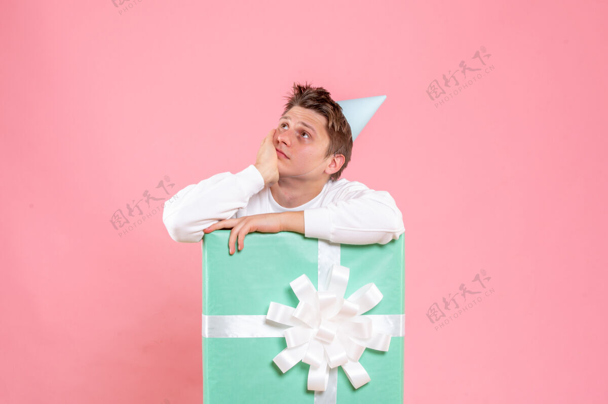 礼物正面图：身穿白色衬衫 头戴鸭舌帽的年轻男性 在粉色背景上呈现思考礼物白色正面