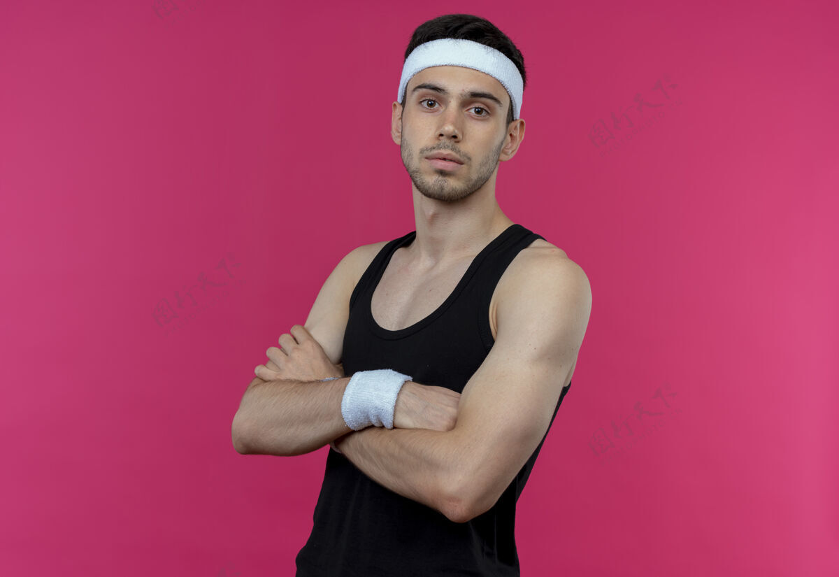 胸部戴着头巾的年轻运动型男子 严肃的脸 双臂交叉放在胸前 超过粉色长相站立脸