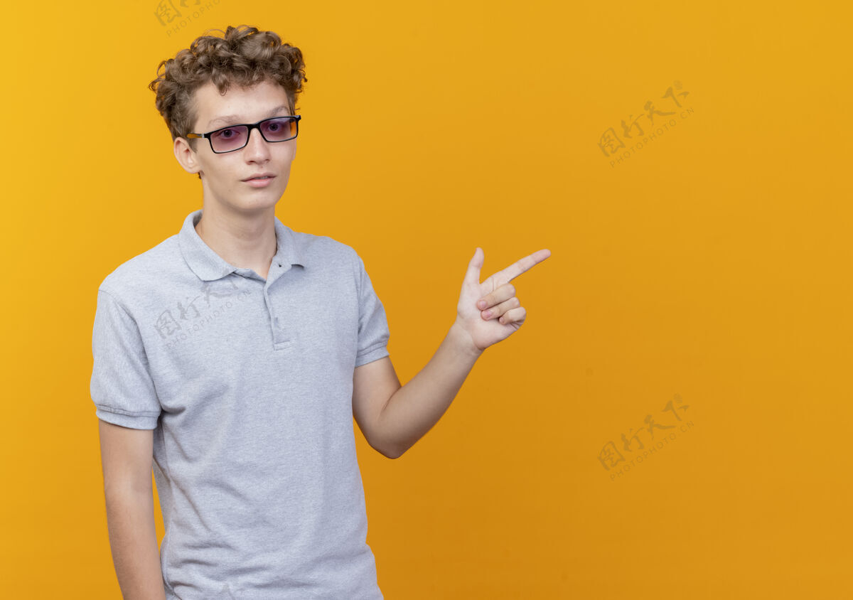 黑色戴着黑眼镜的年轻人穿着灰色马球衫 严肃的脸用手指着橙色的一边衬衫看壁板