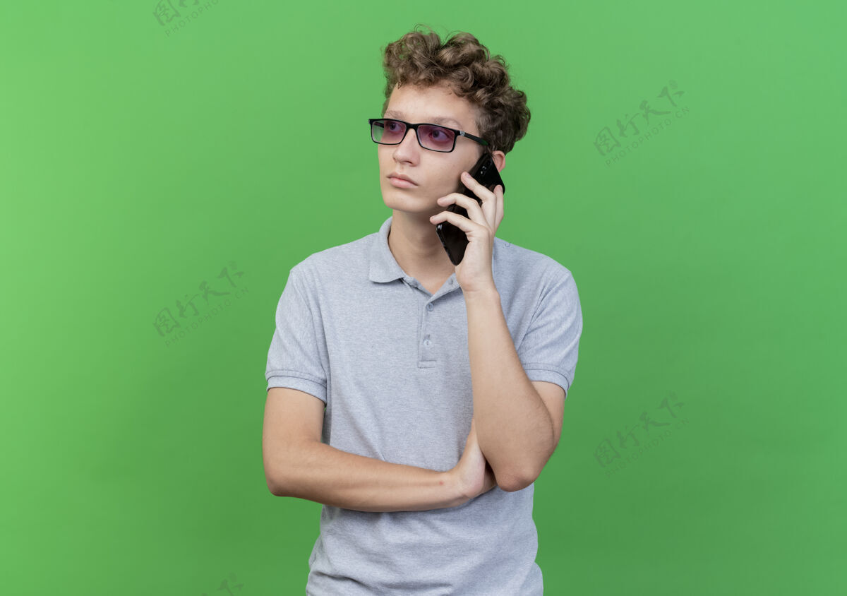 穿戴着黑眼镜 穿着灰色马球衫的年轻人在讲手机 脸上露出严肃的表情看脸说话