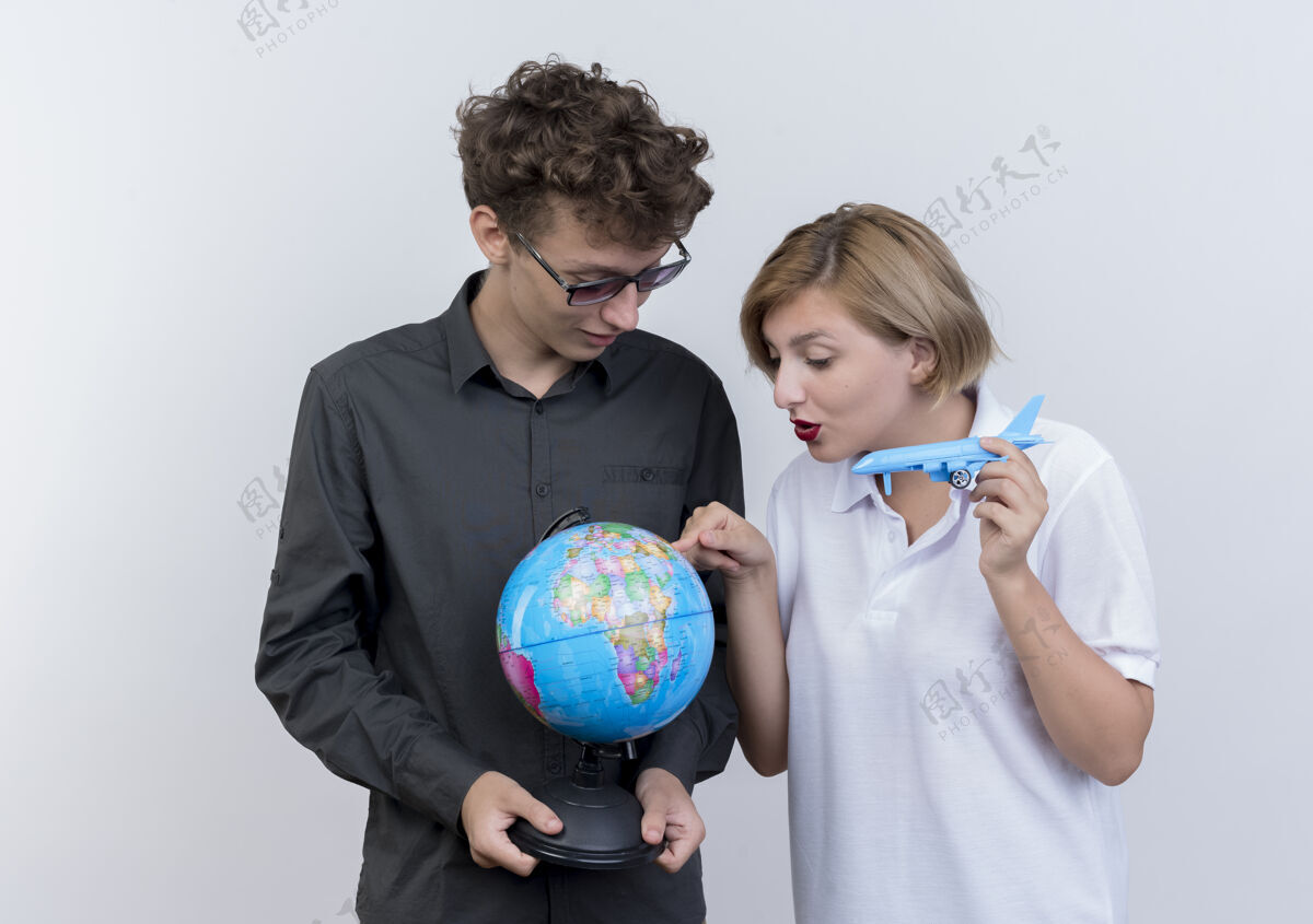 一起一对快乐的年轻游客 一男一女抱着地球仪和玩具飞机在白色上空飞过游客地球仪女人