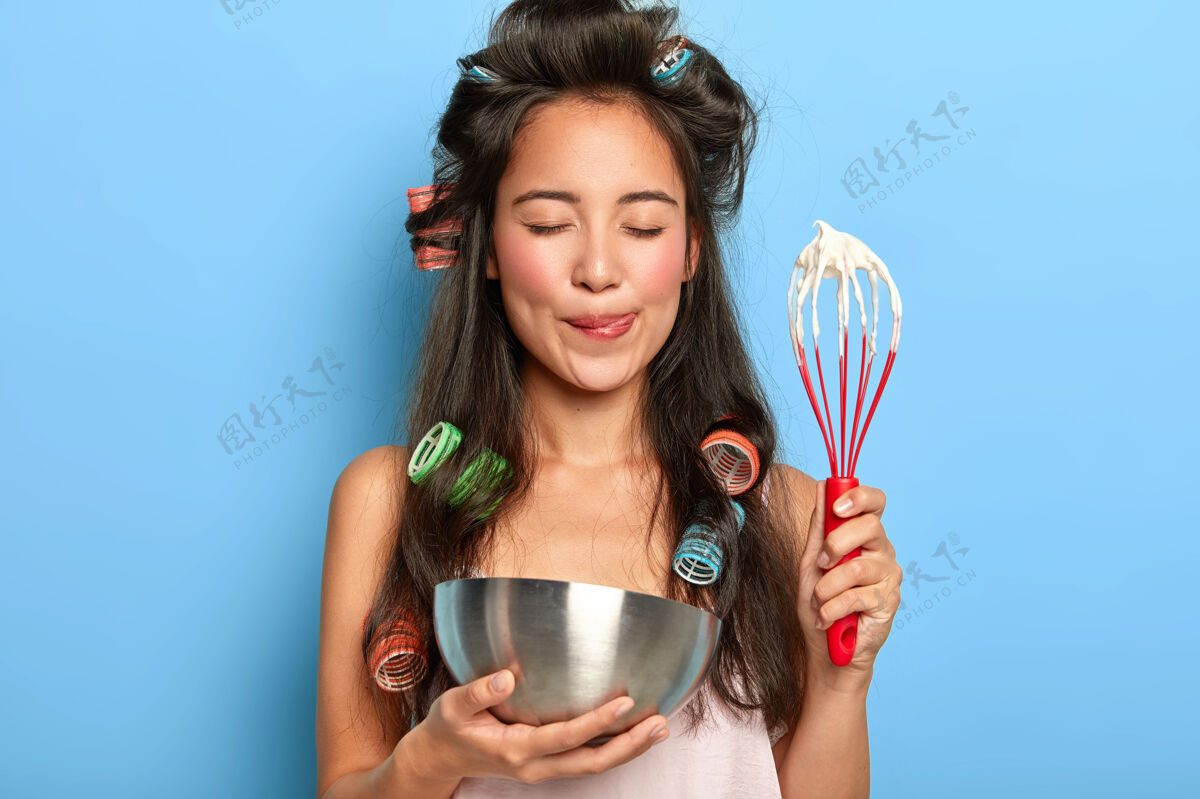 发型满意的黑发女人在碗里搅拌酸奶油 戴着卷发器品尝胭脂女人