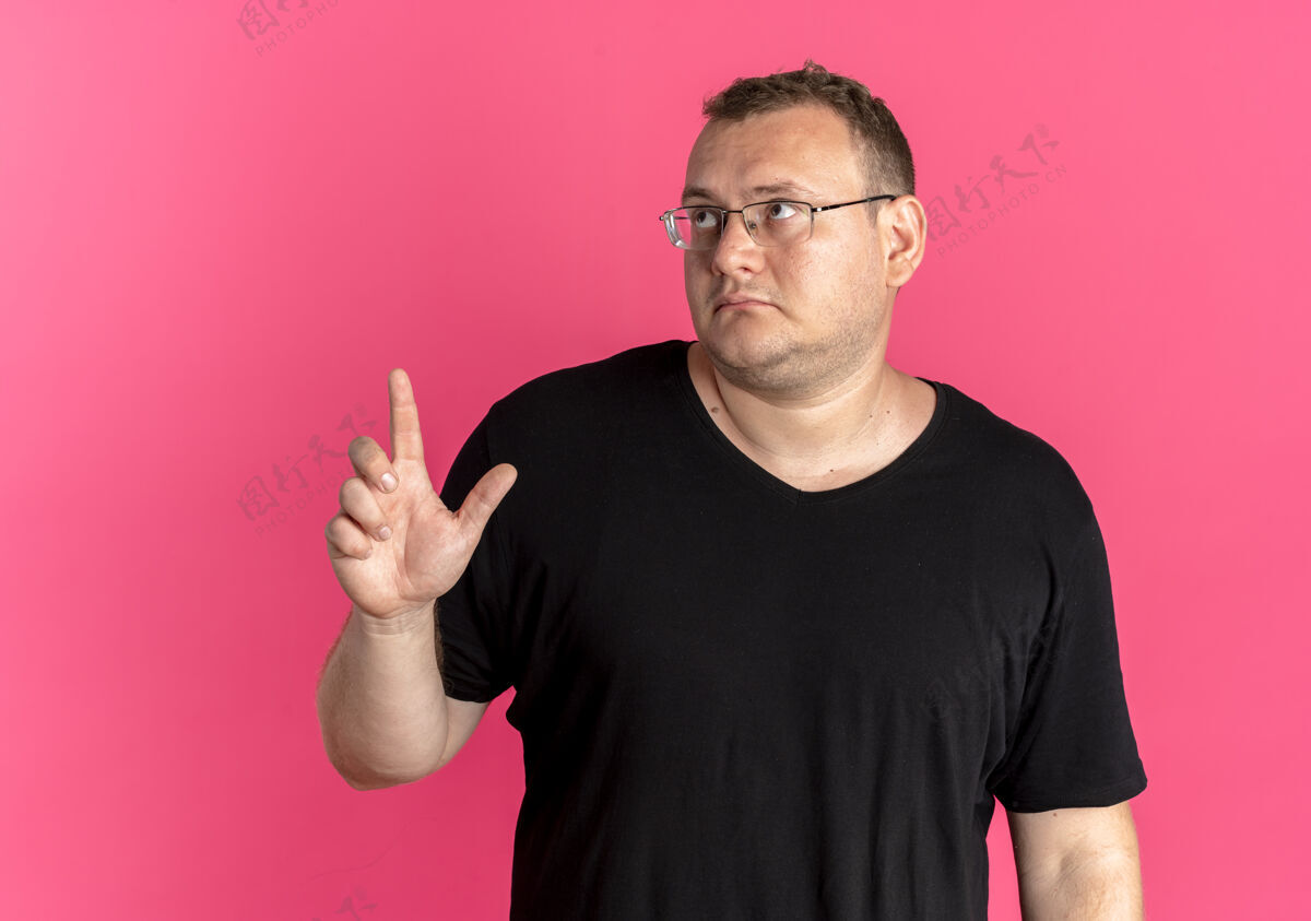 黑色一个戴眼镜 身穿黑色t恤衫的超重男子 一边看一边伸出食指 要求在粉色衣服上稍等片刻粉色T恤问